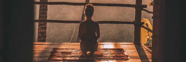 @jareddrice woman in yoga kneeling pose meditating looking away out into jungle forrest at dusk